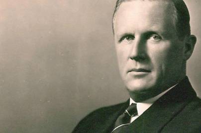 Black-and-white portrait of a serious-looking man in a suit and tie, facing the camera.