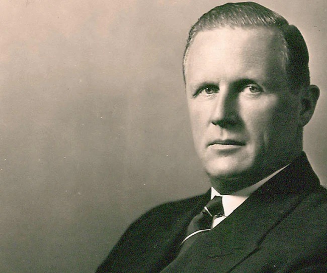 Black-and-white portrait of a serious-looking man in a suit and tie, facing the camera.