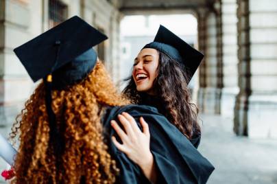 Diverse group of university graduates in caps and gowns celebrating graduation with diplomas outdoors.
